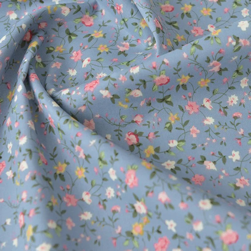 Popeline de coton à fleurs au mètre de Longan Craft France : 100% coton, doux, imprimé floral rose, blanc et jaune sur fond bleu clair avec feuillage vert. Idéal pour quilting, nappes, robes et chemises.
