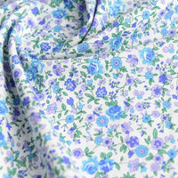 Un gros plan de Popeline de coton à fleurs de Longan Craft France montre un tissu floral doux, 100 % coton, avec des fleurs bleues et violettes et des feuilles vertes, légèrement drapé - idéal pour le quilting, les nappes, les robes ou les chemises.