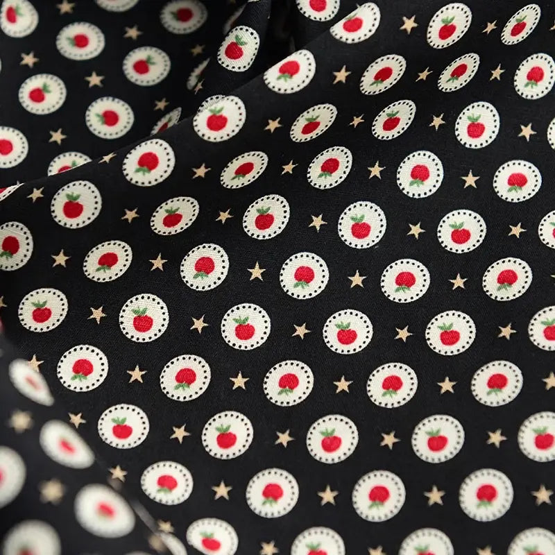 Gros plan sur la Popeline de coton à fleurs au mètre de Longan Craft France, un tissu 100 % coton avec des cercles blancs ornés de fleurs rouges et d'étoiles dorées sur fond noir. Ce tissu doux et légèrement froissé est idéal pour le quilting, les nappes, les robes et les chemises.