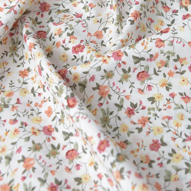 Gros plan sur la Popeline de coton à fleurs au mètre de Longan Craft France, un tissu floral doux 100 % coton avec des fleurs roses, orange et jaunes, idéal pour le quilting, les nappes, les robes et les chemises.