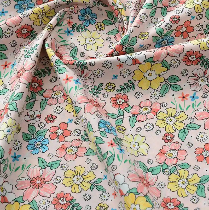 Gros plan sur la Popeline de coton à fleurs au mètre de Longan Craft France, un tissu floral doux 100 % coton avec des fleurs jaunes, roses, bleues et rouges sur fond beige. Légèrement froissé, il est parfait pour le quilting, les nappes, les robes ou les chemises.