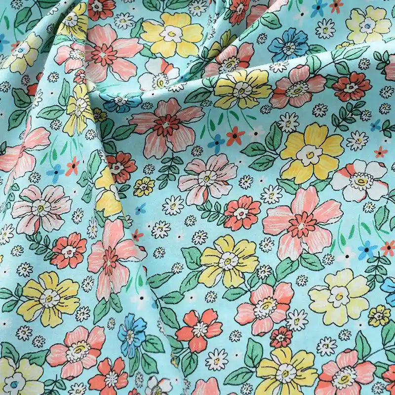 Popeline de coton à fleurs au mètre de Longan Craft France : tissu 100 % coton doux, fond bleu clair, motif floral coloré dense (jaune, rose, rouge, orange et vert). Idéal pour quilting, nappes, robes ou chemises. Légères froissures possibles.