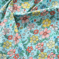 Popeline de coton à fleurs au mètre de Longan Craft France : tissu 100 % coton doux, fond bleu clair, motif floral coloré dense (jaune, rose, rouge, orange et vert). Idéal pour quilting, nappes, robes ou chemises. Légères froissures possibles.