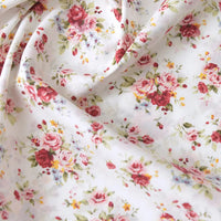 Gros plan sur Popeline de coton à fleurs de Longan Craft France, un tissu floral 100 % coton avec des fleurs roses, rouges et jaunes et des feuilles vertes. Ce tissu de quilting doux est légèrement drapé et texturé, parfait pour les robes ou la décoration.