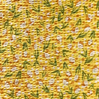 Le Tissu seersucker fleuri au mètre de Longan Craft France est un seersucker de coton vintage jaune avec de petites feuilles vertes et des grappes de points blancs dans un motif floral répétitif et uniformément réparti.