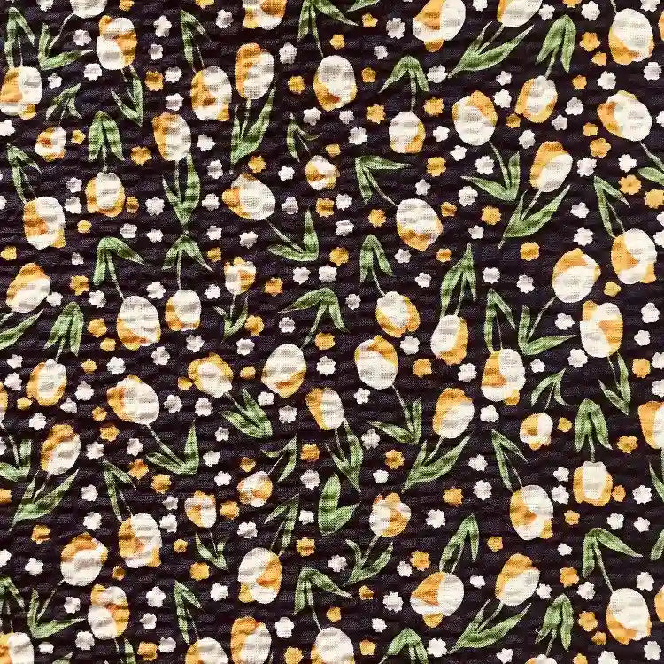Vue détaillée du Tissu seersucker fleuri au mètre de Longan Craft France, un coton léger de style vintage avec un motif floral dense jaune et blanc sur fond noir, avec des feuilles vertes et une finition froissée.
