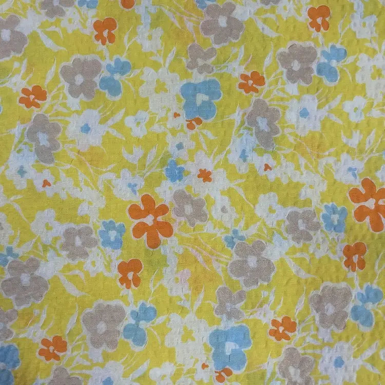 Le Tissu seersucker imprimé floral au mètre de Longan Craft France est un coton léger et respirant qui présente un motif dense de fleurs bleues, orange et beiges sur un fond jaune pour un look vintage vibrant.