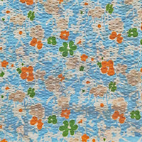 Le Tissu seersucker imprimé floral au mètre de Longan Craft France est un coton seersucker bleu texturé avec un motif floral vintage gaufré en orange, beige et vert.