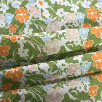 Gros plan sur le Tissu seersucker imprimé floral au mètre de Longan Craft France, un seersucker gaufré en coton léger avec un fond vert et des fleurs vintage orange, rose pâle et bleu clair avec des tiges et des feuilles blanches.