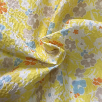 Gros plan sur le Tissu seersucker imprimé floral au mètre de Longan Craft France, un coton léger gaufré à l'imprimé floral vintage orange, bleu, beige et blanc. La texture froissée offre un aspect doux et respirant.