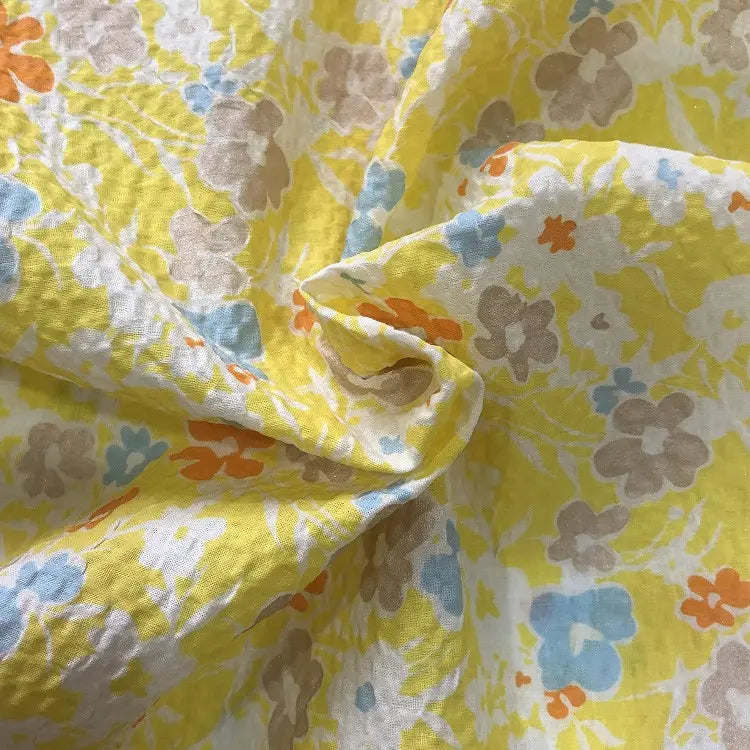 Gros plan sur le Tissu seersucker imprimé floral au mètre de Longan Craft France, un coton léger gaufré à l'imprimé floral vintage orange, bleu, beige et blanc. La texture froissée offre un aspect doux et respirant.