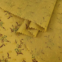 Plumetis en voile jacquard jaune de Longan Craft France, à la texture subtilement pointillée et à l'imprimé floral de fines branches feuillues. Bords coupés en zigzag, parfaits pour les robes d'été. Tissu au mètre pour confection et couture.