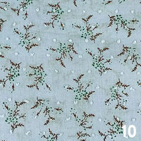 Le Tissu voile jacquard plumetis floral au mètre de Longan Craft France présente un voile de coton bleu clair avec de petites branches brunes, des feuilles vertes et des points blancs - parfait pour les robes d'été. Le chiffre "10" apparaît en blanc en bas à droite.