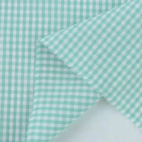 Gros plan sur le Tissu popeline vichy au mètre de Longan Craft France, un vichy 100 % coton bleu clair et blanc à petits carreaux et à bords effilochés, idéal pour les chemises, les robes ou les nappes d'été.