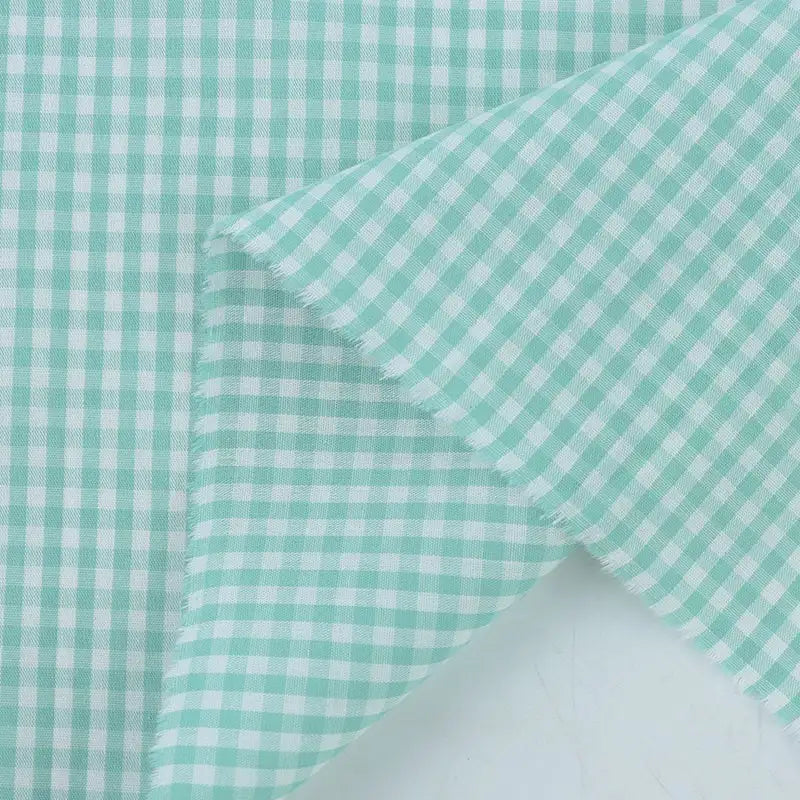 Gros plan sur le Tissu popeline vichy au mètre de Longan Craft France, un vichy 100 % coton bleu clair et blanc à petits carreaux et à bords effilochés, idéal pour les chemises, les robes ou les nappes d'été.