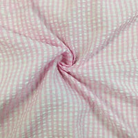 Un gros plan du Seersucker vichy au mètre de Longan Craft France montre sa texture froncée rose et blanche, torsadée au centre pour mettre en valeur la matière seersucker à carreaux typique de ce tissu léger.