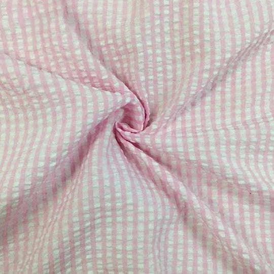 Un gros plan du Seersucker vichy au mètre de Longan Craft France montre sa texture froncée rose et blanche, torsadée au centre pour mettre en valeur la matière seersucker à carreaux typique de ce tissu léger.