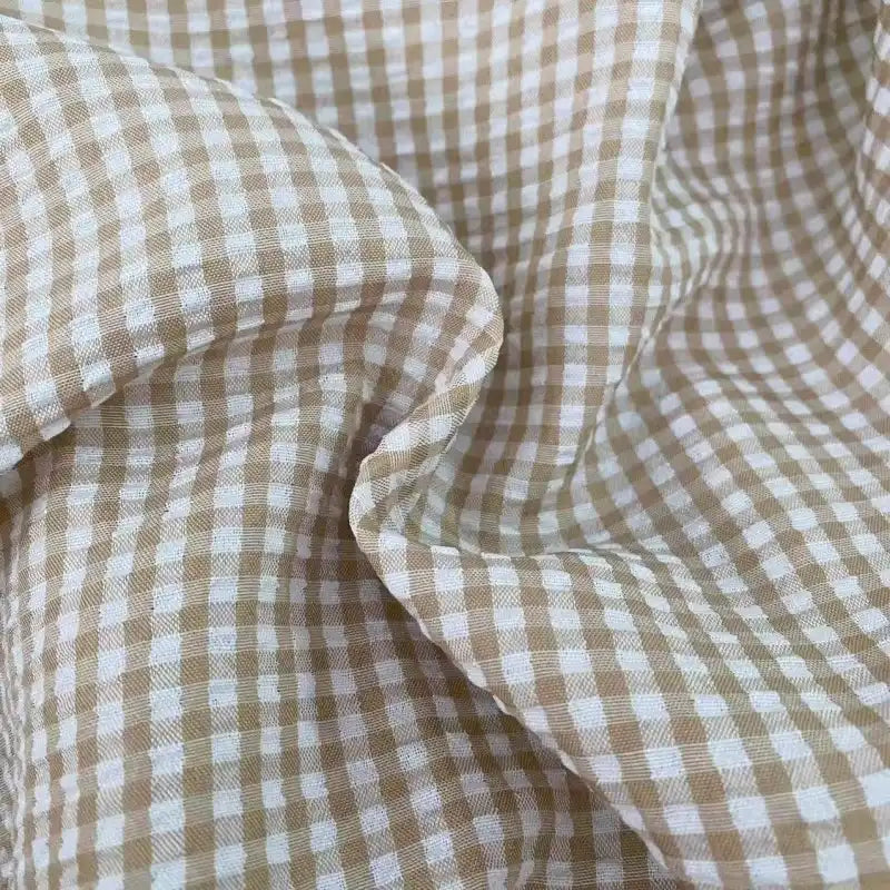 Gros plan sur le Seersucker vichy au mètre de Longan Craft France : un seersucker à carreaux beige et blanc, légèrement froissé, qui présente des petits carrés issus de rayures verticales et horizontales régulièrement espacées.