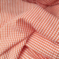 Le Seersucker vichy au mètre de Longan Craft France est présenté en orange et blanc, avec des petits carreaux et une texture légère, légèrement froissée, avec des plis doux.