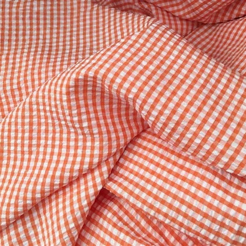 Le Seersucker vichy au mètre de Longan Craft France est présenté en orange et blanc, avec des petits carreaux et une texture légère, légèrement froissée, avec des plis doux.