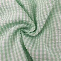 Gros plan sur le Seersucker vichy au mètre de Longan Craft France : tissu carreaux vert clair et blanc au pli froissé et tourbillonnant. Ce tissu seersucker froncé a une texture douce et légère.