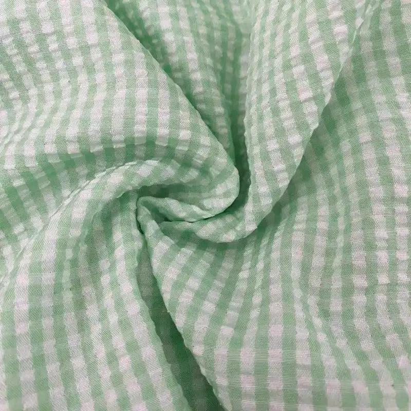Gros plan sur le Seersucker vichy au mètre de Longan Craft France : tissu carreaux vert clair et blanc au pli froissé et tourbillonnant. Ce tissu seersucker froncé a une texture douce et légère.