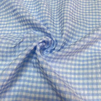 Un gros plan du Seersucker vichy au mètre de Longan Craft France montre un tissu seersucker bleu clair et blanc avec un motif à carreaux, tourbillonné au centre pour un aspect texturé et froissé.