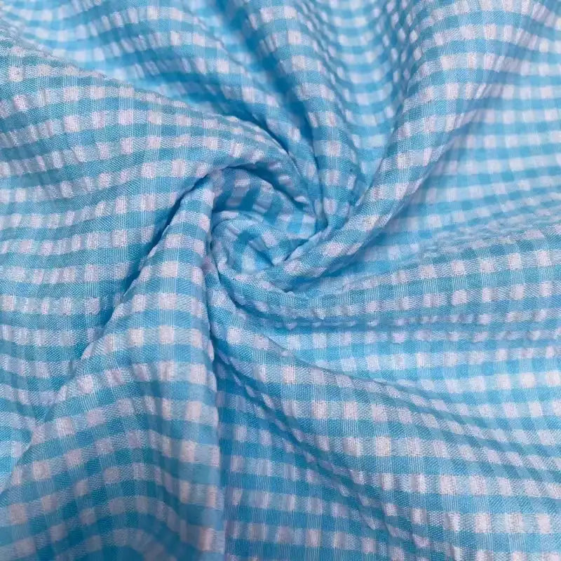 Gros plan sur le Seersucker vichy au mètre de Longan Craft France, un seersucker à carreaux bleu clair et blanc à petits carreaux, torsadé pour mettre en valeur sa texture froncée et son toucher léger et doux.
