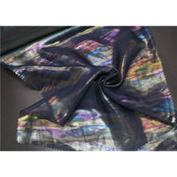 Un morceau de Mousseline irisée au mètre de Longan Craft France, une mousseline de polyester foncé métallisée avec un motif multicolore irisé, est étalé sur une table avec une partie torsadée en une spirale lâche au centre.