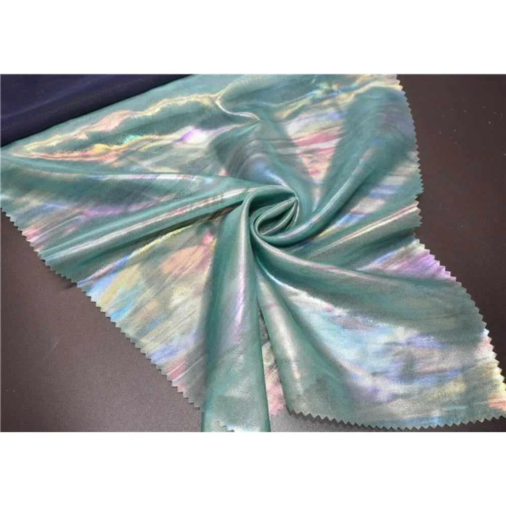 Un morceau de Mousseline irisée au mètre de Longan Craft France, un tissu métallisé haut de gamme en polyester multicolore, est étalé et rassemblé au centre, avec des bords coupés en zigzag pour les créations DIY.