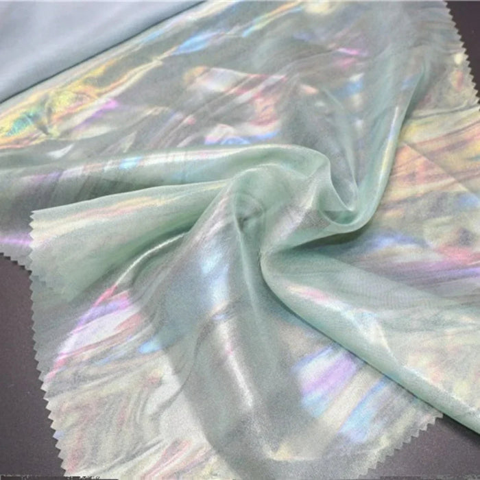 Un morceau de Mousseline irisée au mètre de Longan Craft France est disposé sur une surface sombre, rassemblé au centre pour mettre en valeur sa texture polyester brillante et semi-transparente et ses douces teintes pastel, parfaites pour les projets de bricolage.