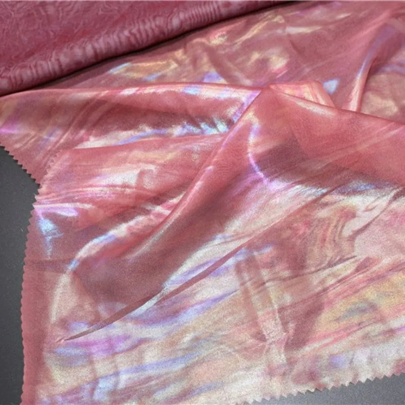 Un morceau de Mousseline irisée au mètre de Longan Craft France est posé à plat avec un coin plié, révélant des teintes arc-en-ciel brillantes et une texture ondulée - parfaite pour les projets de bricolage avec sa finition luxueuse en polyester métallisé.