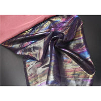 Un morceau de Mousseline irisée au mètre de Longan Craft France, une mousseline de polyester multicolore et brillante, est drapé sur un tissu noir à côté d'un tissu rose uni, reflétant des nuances de bleu, de violet et d'or - parfait pour les fournitures de bricolage.