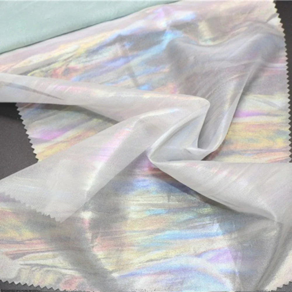 La Mousseline irisée au mètre de Longan Craft France est une mousseline de polyester semi-transparente et lisse, aux reflets arc-en-ciel subtils, parfaite pour les projets de bricolage et les effets de lumière chatoyants.