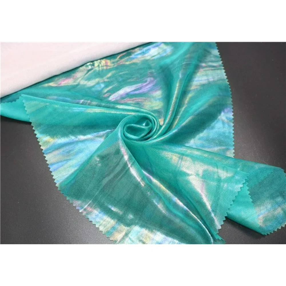 Un morceau de polyester brillant Mousseline irisée au mètre de Longan Craft France, avec des bords rosés, est posé à plat et froncé à un coin au centre - parfait pour les projets de couture DIY.