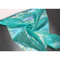 Un morceau de polyester brillant Mousseline irisée au mètre de Longan Craft France, avec des bords rosés, est posé à plat et froncé à un coin au centre - parfait pour les projets de couture DIY.