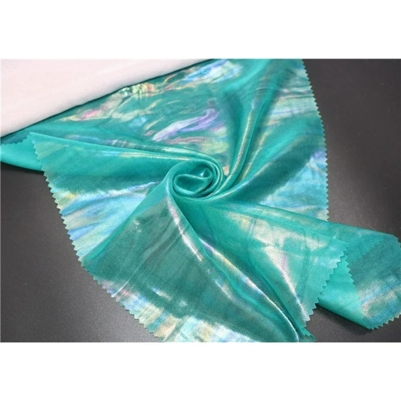 Un morceau de polyester brillant Mousseline irisée au mètre de Longan Craft France, avec des bords rosés, est posé à plat et froncé à un coin au centre - parfait pour les projets de couture DIY.