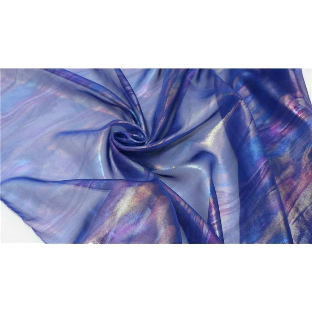 Un gros plan de la Mousseline irisée au mètre de Longan Craft France, ce tissu mousseline polyester métallisé présente un tourbillon central et des reflets irisés bleus, violets, roses et dorés - idéal pour les fournitures de bricolage.