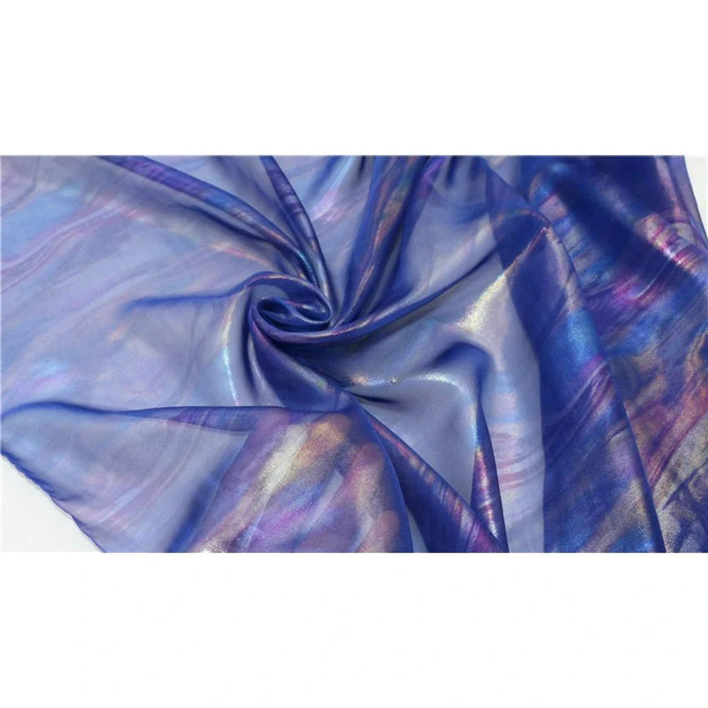 Un gros plan de la Mousseline irisée au mètre de Longan Craft France, ce tissu mousseline polyester métallisé présente un tourbillon central et des reflets irisés bleus, violets, roses et dorés - idéal pour les fournitures de bricolage.