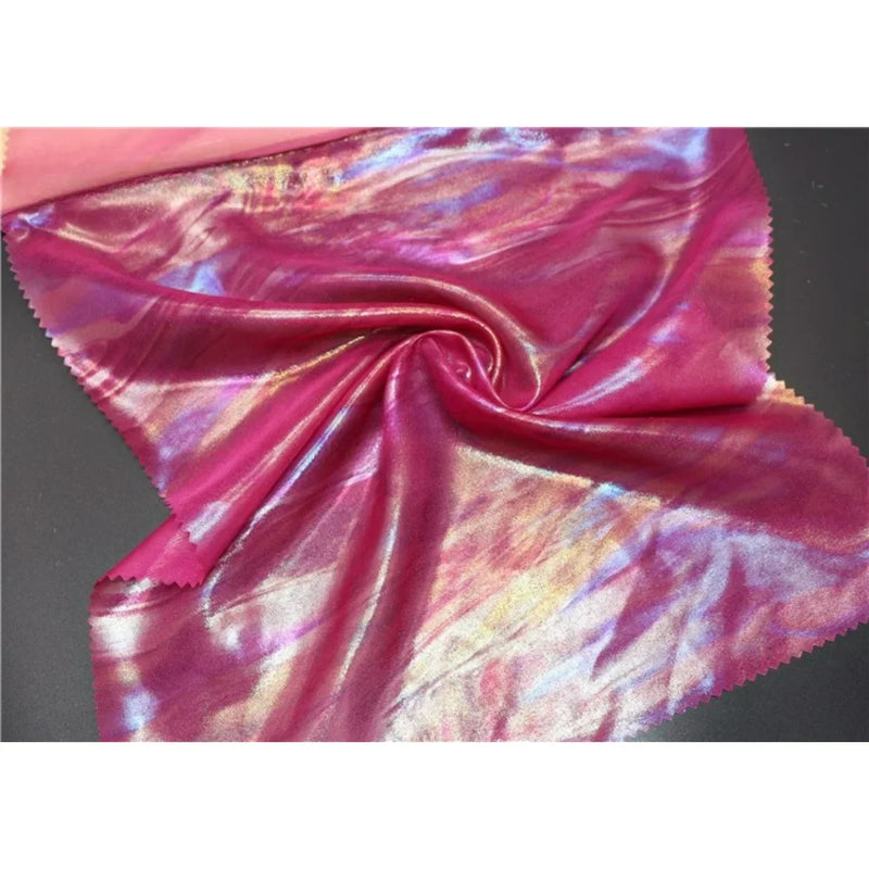 Un morceau de Mousseline irisée au mètre de Longan Craft France, une mousseline métallique de polyester brillante aux couleurs rose, violet, bleu et or avec des bords rosés, est étalé à plat avec un tourbillon au centre - parfait pour les fournitures de bricolage.
