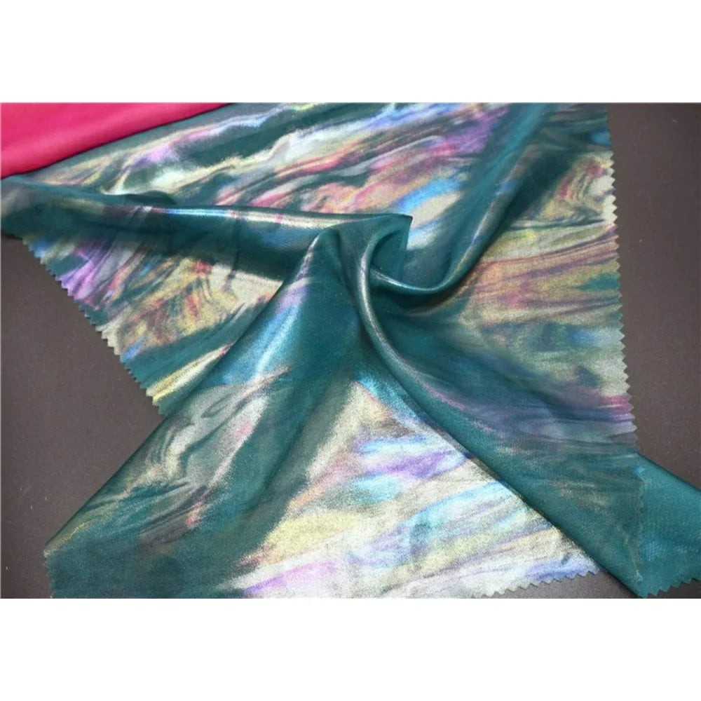 Une mousseline irisée au mètre de Longan Craft France, avec une surface de mousseline de polyester métallique multicolore, est présentée sur un fond sombre avec un soupçon de tissu rose vif visible dans le coin.