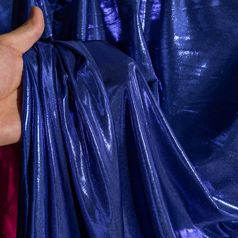 Une main rassemble une section de Lamé métallique liquide de Longan Craft France, mettant en valeur le tissu bleu brillant, réfléchissant et lisse, idéal pour les costumes de scène, les robes et la couture.