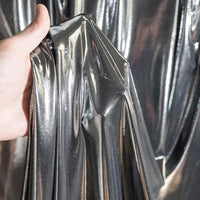 Une main présente le Lamé métallique liquide au mètre de Longan Craft France, dont le tissu brillant et extensible capte la lumière - parfait pour les costumes de scène, les robes de soirée et la couture avec un reflet lisse et réfléchissant.