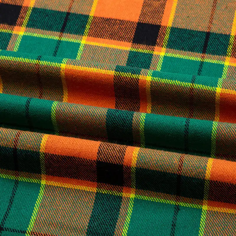 Gros plan sur la Flanelle de coton à carreaux au mètre de Longon Craft France, tissu doux à motif tartan orange, vert, jaune et noir, légèrement plié avec de douces marques horizontales. Idéal pour chemises, robes ou pantalons d'automne.