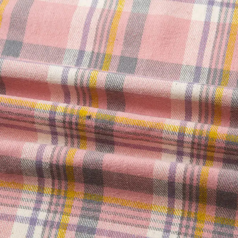Gros plan sur la flanelle de coton à carreaux au mètre de Longon Craft France : motif écossais rose avec des lignes jaunes, grises et violettes. Ce tissu doux et confortable est parfait pour les chemises, les robes et les pantalons d'automne.