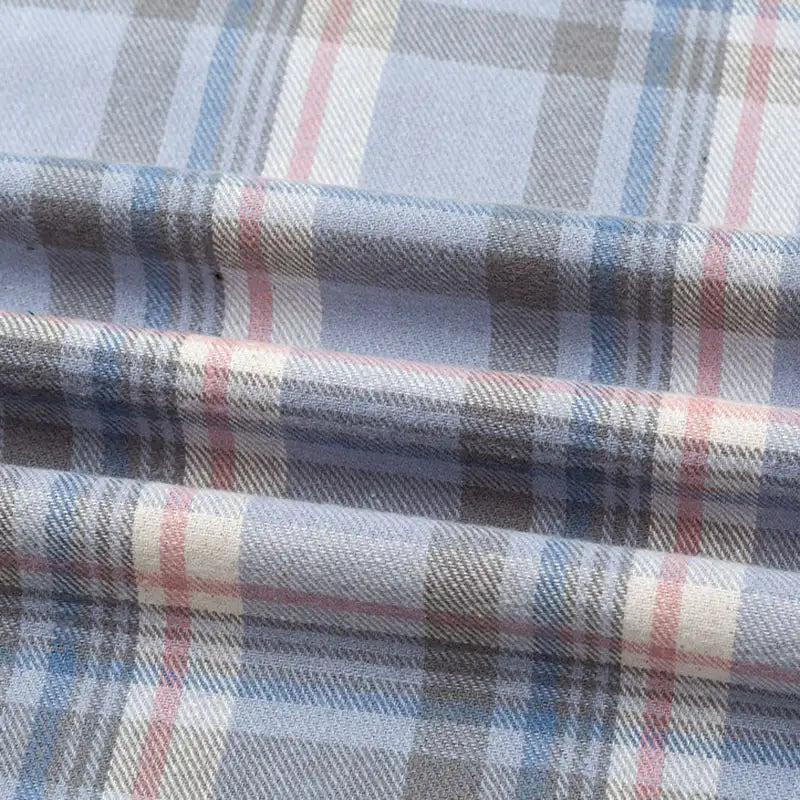 Gros plan sur la Flanelle de coton à carreaux au mètre de Longon Craft France, montrant une texture douce et des plis visibles. Ce tissu d'automne confortable présente des rayures bleues, grises et rouges entrecroisées, idéales pour les chemises, les robes ou les pantalons.