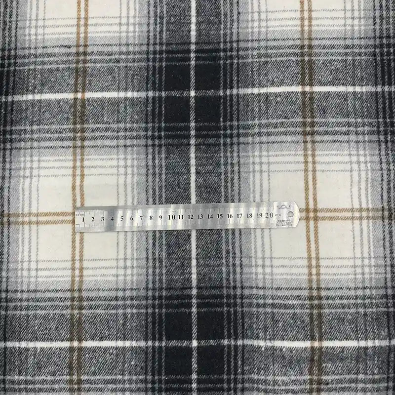 Une règle en métal repose sur le Tissu en flanelle à carreaux pour l'automne au mètre de Longon Craft France, un tissu polyester-coton doux et confortable, idéal pour robes, chemises ou couture d'hiver.