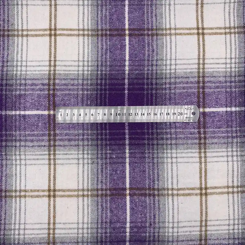 Une règle métallique indiquant les centimètres et les millimètres est posée sur le tissu en flanelle à carreaux pour l'automne au mètre de Longon Craft France, un tissu en polyester-coton idéal pour les peignoirs, les chemises et la couture d'hiver.