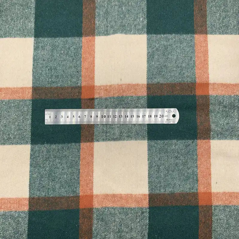 Une règle en métal indiquant les centimètres et les millimètres repose sur le tissu en flanelle à carreaux pour l'automne-un tissu polyester-coton confortable, idéal pour robes, chemises ou vêtements d'hiver de Longon Craft France.