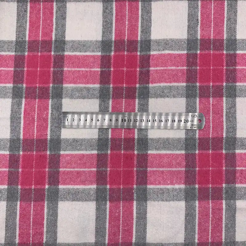 Une règle en métal est posée sur le tissu en flanelle à carreaux pour l'automne au mètre de Longon Craft France, un tissu en polyester-coton rose, gris et blanc idéal pour les robes, les chemises et les projets de couture d'automne. La règle indique 0-20 cm.
